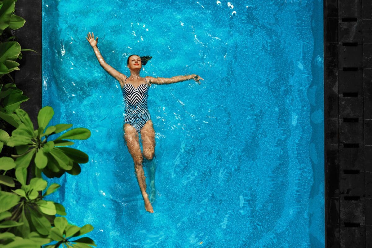 Woman In Pool Water. Beautiful Happy Girl With Sexy Fit Body Relaxing, Floating In Swimming Pool.