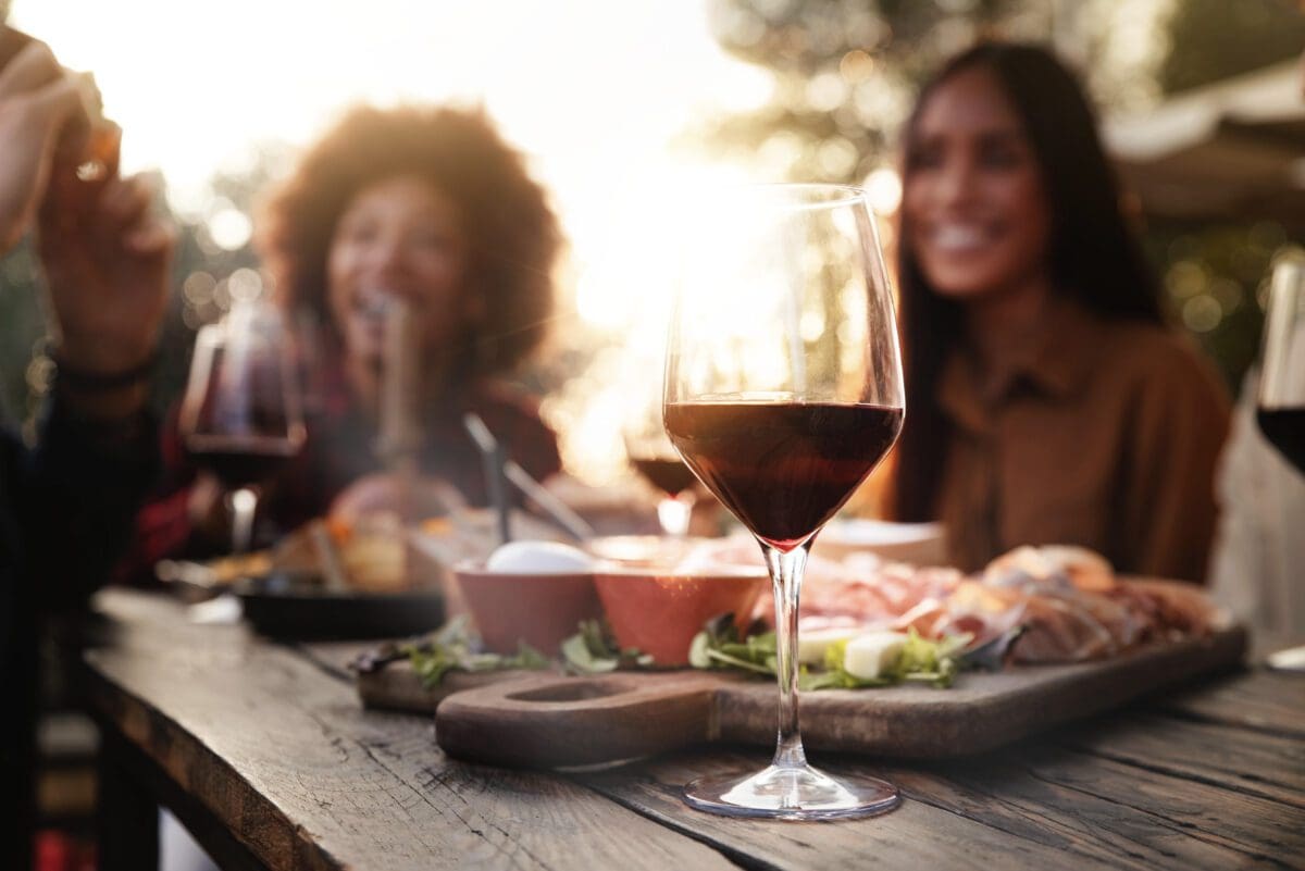 Group of friends having fun at a private maui chef experience - Multiracial people cheering red wine sitting outside at table