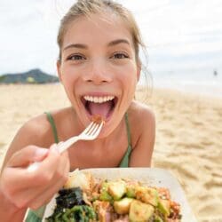 Funny woman eating salad healthy meal on beach